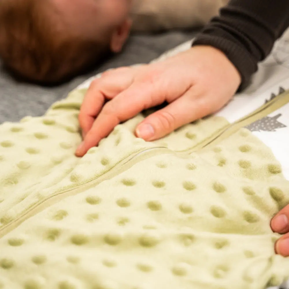 Forældres hånd rører ved tyndesovepose LumiSack fra LilleLumi mens baby ligger ned